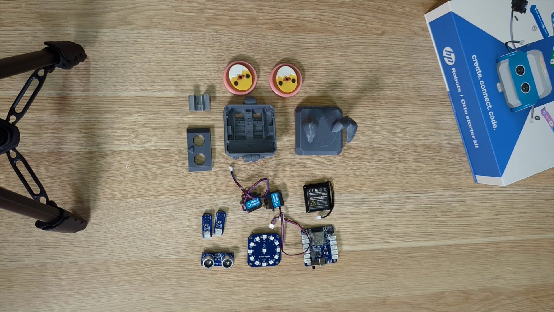 Flat lay of the HP Otto robot starter kit components, including 3D-printed parts, sensors, wheels, and a controller board on a wooden surface.